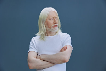 elderly man with long white hair and beard, thoughtful expression, arms crossed, casual white t shirt, studio shot, portrait photo capturing wisdom and introspectionの写真素材