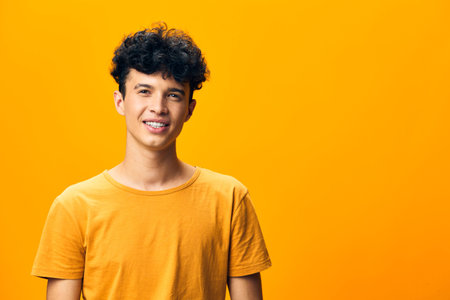 smiling young man with curly hair against a bright orange background wearing a casual yellow t shirt, exuding a cheerful and positive vibe, perfect for upbeat themesの写真素材