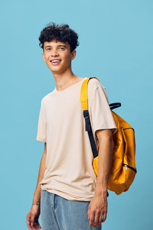 Young man smiling with a yellow backpack against a blue background, casual attire, showcasing a cheerful and relaxed vibe Perfect for lifestyle and fashion conceptsの写真素材
