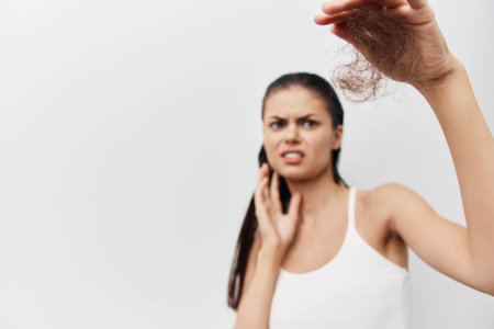 Hair loss, concern, health issues A distressed young woman holding a clump of hair with a worried expression, standing against a neutral background, expressing anxiety about hair thinningの写真素材