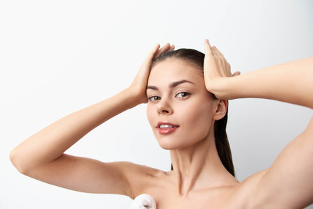 Portrait of a young woman with long, straight hair posing against a white background, showcasing natural beauty and skincare. Relaxed expression and hands on her head.の写真素材