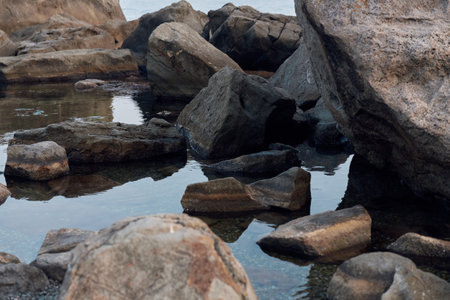 Tranquil ocean scene with clear water, rocks, and boulders scattered along the shoreの写真素材