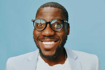 Happy man smiling against a blue background, wearing glasses and a light blazer His joyful expression conveys positivity and confidence, ideal for lifestyle and fashion themesの写真素材
