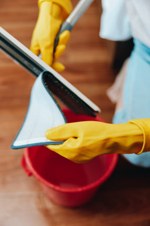 Person in yellow gloves cleaning floor with sponge and cloth near buckets of waterの写真素材