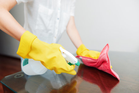 Woman in rubber gloves cleaning table with rag and bottle of cleaning solutionの写真素材