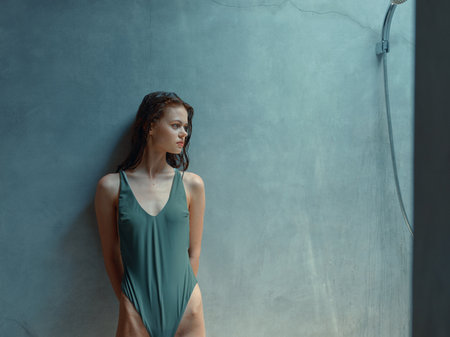 Stylish woman in green swimsuit posing in front of vibrant blue wallの写真素材