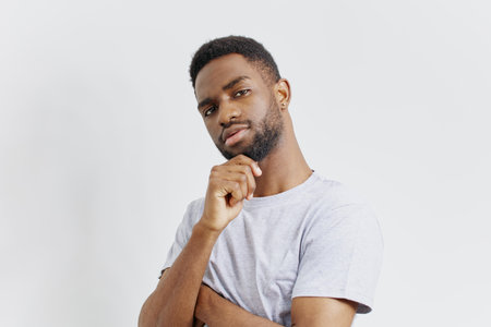Thoughtful african american man in grey tshirt posing with hand on chin, contemplating ideas or decisionsの写真素材