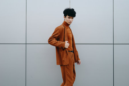 Stylish young man in a brown suit standing against a gray geometric background His confident pose emphasizes contemporary fashionの写真素材