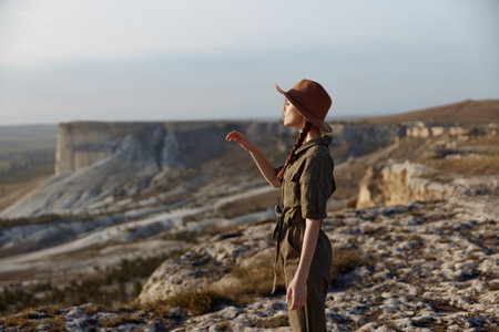 Woman in brown hat standing on top of mountain overlooking valley below in a travel adventure sceneの写真素材