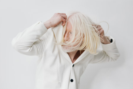 White fashion, modern aesthetics A man with long white hair pulls a hoodie over his head against a clean, light background Stylish and contemporary vibeの写真素材