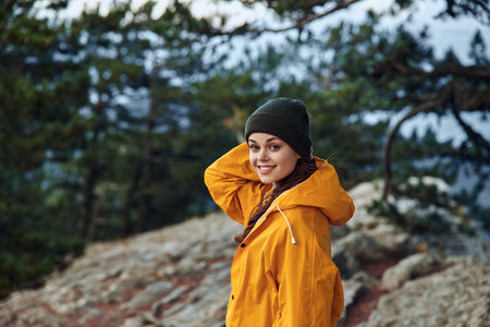 Woman in Yellow Raincoat Standing on Top of Mountain Surrounded by Lush Treesの写真素材