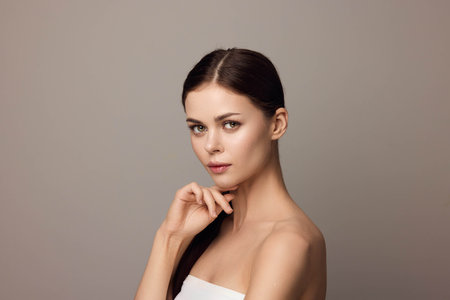 Beautiful young woman with hands on chin looking at camera on gray background with copy spaceの写真素材