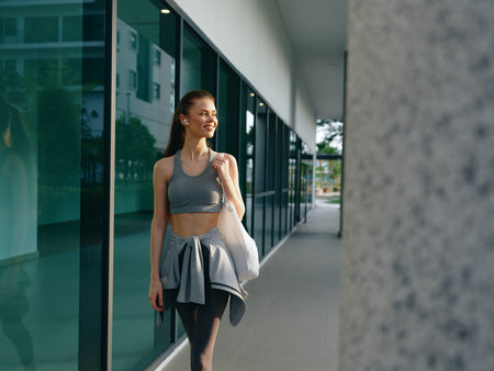 Young woman in sportswear walking outside in a modern urban setting with large glass windowsの写真素材