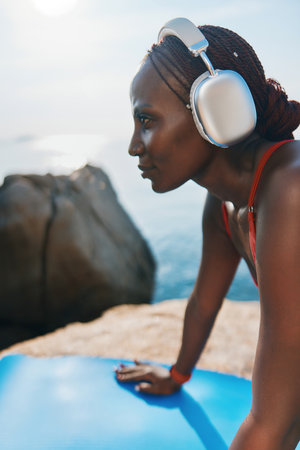 A young woman in headphones enjoying a serene outdoor moment on a yoga mat, gazing into the distance by the ocean The scene captures tranquility and connectionの写真素材