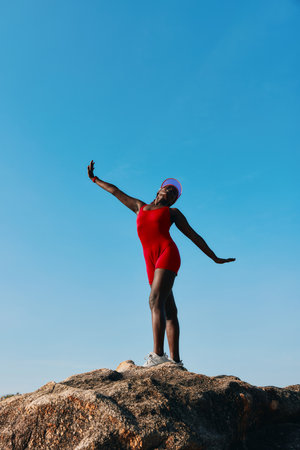 A woman in a red swimsuit posing confidently on a rock against a clear blue sky Her joyful expression emphasizes freedom and vitalityの写真素材