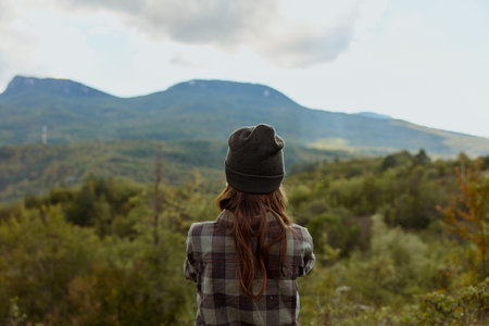 A woman in plaid shirt and beanie marveling at majestic mountain range during adventurous outdoor...