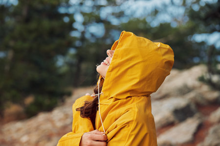 A woman in a yellow raincoat exploring the rocky hill and trees in the background during her nature tripの写真素材