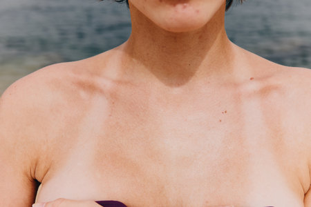 Close up of a womans bare chest with the ocean and sun in the backgroundの写真素材