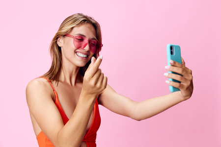 Gorgeous young woman in swimsuit capturing a selfie with her phone against a vibrant pink backgroundの写真素材