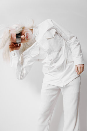 Fashionable model with white hair in a striking pose, wearing a stylish white outfit, showcasing creativity and uniqueness against a plain light backgroundの写真素材