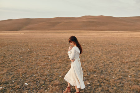 Woman in white dress standing in open field with mountains in background serene beauty of nature and travel exploration conceptの写真素材