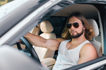Stylish man in sunglasses inside a car, showcasing a confident pose against a light interior...