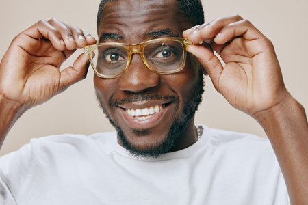 Smiling young man with glasses expressing joy and confidence in a casual outfit against a neutral background, showing positive emotions and a friendly demeanorの写真素材