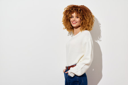 woman with curly hair, smiling, stylish outfit, white wall background, casual fashion, happiness and...