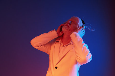 Elderly man enjoying music with headphones in a vibrant colored background, featuring blue and orange hues, capturing emotions of relaxation and joy through the contrast of colorsの写真素材