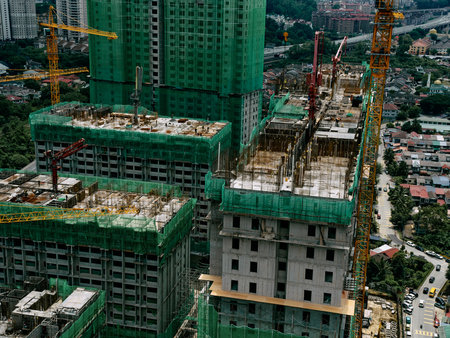Construction site of a high rise building with cranes and scaffolding Green mesh covers the...