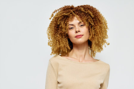 Beautiful woman with curly hair against a light background, showcasing natural beauty and confidence Soft lighting enhances her features and creates an inviting atmosphereの写真素材