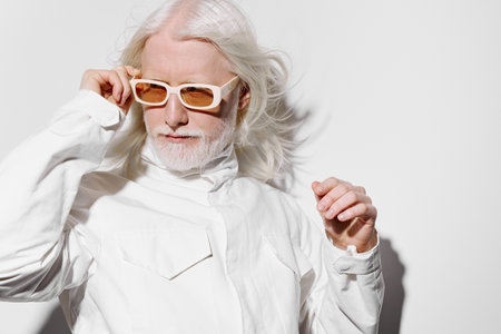 elderly man with white hair and beard wearing stylish sunglasses against a minimalistic white background, exuding confidence and modernity with a fashionable outfit and poseの写真素材