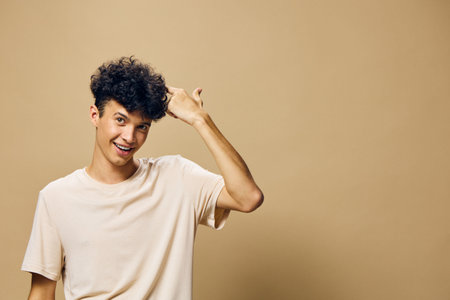 Young man with curly hair smiling playfully on a solid neutral background, showcasing casual attire and a cheerful expression Perfect for lifestyle or youth conceptsの写真素材