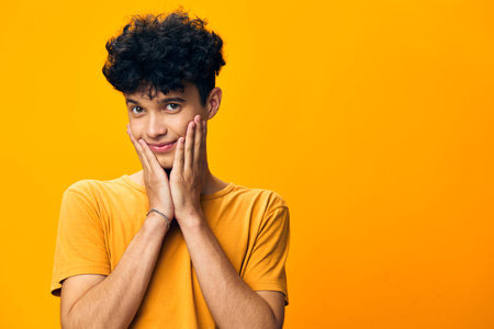 Happy young man with curly hair expressing joy and surprise against a vibrant orange background,...