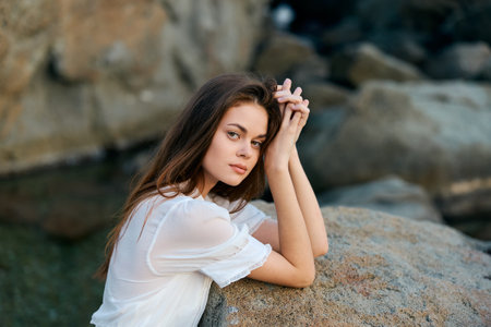 serene beauty young woman sitting gracefully on a rock by the sea, contemplating the horizonの写真素材