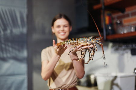 Woman holding lobster in front of kitchen counter with red pots and pansの写真素材