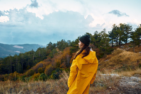 A woman in a yellow raincoat enjoying the majestic view of the mountains while standing on a hilltopの写真素材