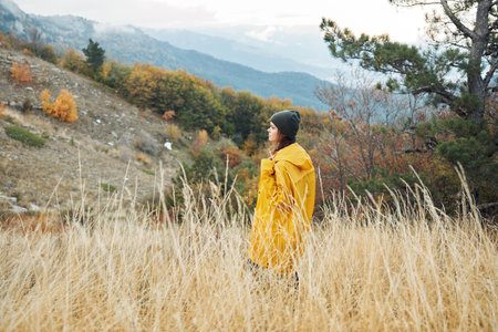 Woman in yellow raincoat enjoying nature a scenic view of mountains and tall grass