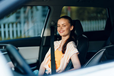 cheerful young woman sitting in a car with a smile, showcasing safety and comfort in a modern vehicle, bright interior with daylight filtering through the windows, joyful expressionの写真素材