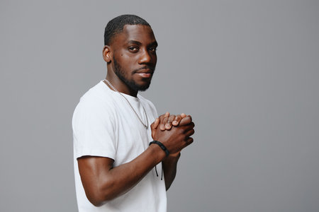 Stylish young man in casual white shirt with hands clasped, looking confidently at the camera...