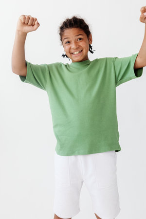 Excited young boy in stylish green tshirt and white shorts raising arms in celebrationの写真素材