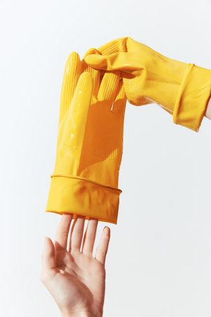 Yellow rubber gloves held up by hands on a white background, one glove on each handの写真素材