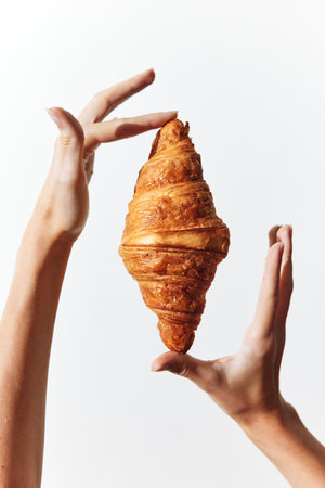 Hands holding croissant on white background, croissant in center
