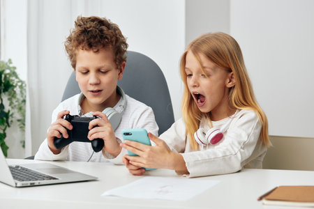 Children studying together at home with their laptops and headphones, immersed in elearning and...