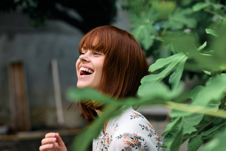 Joyful redhead woman laughing in front of vibrant tree with lush green leaves