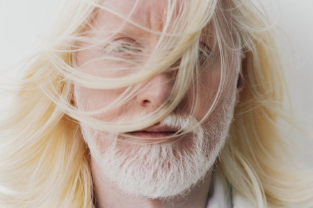 Portrait of a person with long, flowing blonde hair and a white beard, soft focus, light neutral background, capturing a serene and ethereal atmosphere with gentle movementの写真素材