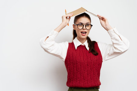Girl with glasses, holding a book above her head, excited expression, wearing a red sweater Light...