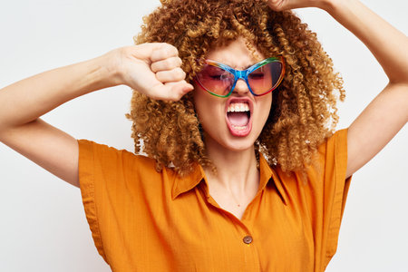 Stylish woman with curly hair wearing colorful sunglasses and an orange shirt, expressing strong...