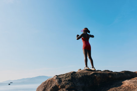 Woman in a swimsuit standing on a rock by the sea, enjoying the beautiful view The sky is clear and blue, creating a serene atmosphereの写真素材