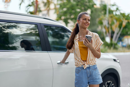 Young woman standing by a car, smiling, holding a smartphone, casual summer outfit, urban...